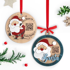 Puede incluir: Dos adornos navideños de madera con diseños de Papá Noel. Uno muestra a Papá Noel con un saco, el otro tiene la palabra "Santa" en escritura. Ambos tienen códigos QR y leen "Scan to track Santa". Se adjuntan cintas rojas.
