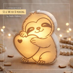 May include: A glowing, light-coloured sloth-shaped lamp holding a heart with a heart-shaped cutout. The lamp has a smiling face and is lit from within. Text on the image reads "STL & 3MF FOR 3D PRINTING by Studio Wallaby."