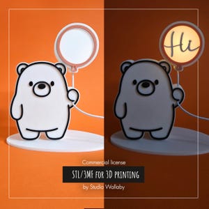 May include: A white bear-shaped lamp with a black outline, holding a balloon-shaped light. The balloon light has a pink border and the word "Hi" written on it. The lamp is on a white base, with a wire extending from the base.
