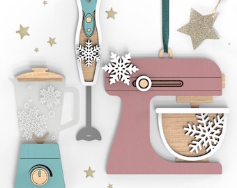 May include: A set of three wooden kitchen appliance ornaments, including a blender, a stand mixer, and an immersion blender. Each ornament is decorated with a snowflake design and has a rustic, farmhouse style.