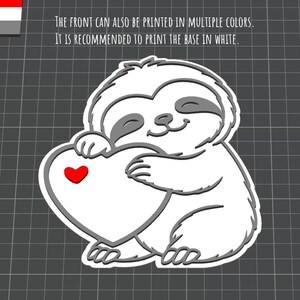 May include: A white and gray cartoon sloth holding a white heart with a red heart in the center. The sloth has closed eyes and a smiling expression. The text on the image says, "THE FRONT CAN ALSO BE PRINTED IN MULTIPLE COLORS. IT IS RECOMMENDED TO PRINT THE BASE IN WHITE."