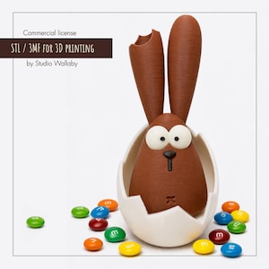 May include: A brown Easter bunny figure emerging from a white eggshell, surrounded by colorful candies. The bunny has large white eyes and a small black nose. The image includes the text "STL / 3MF FOR 3D PRINTING".
