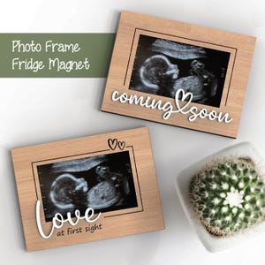 Puede incluir: Dos marcos de fotos de madera con imágenes de ultrasonido en su interior. El marco superior tiene el texto "coming soon" con un corazón. El marco inferior tiene el texto "love at first sight" con dos corazones.
