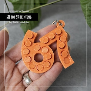 May include: Orange 3D-printed keychain in the shape of the number "61". The keychain has a series of circular studs, and a small metal ring for attachment. The text "STL FOR 3D PRINTING" and "by Studio Wallaby" is visible.