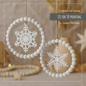 Puede incluir: Dos adornos blancos de copo de nieve con un diseño de círculo de cuentas, colgando de una cuerda. Los adornos tienen el texto "STL FOR 3D PRINTING by Studio Wallaby" y son para licencia comercial.