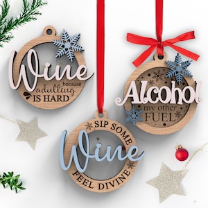Könnte beinhalten: Drei runde Weihnachtsbaumschmuck aus Holz mit rotem Band. Die Anhänger haben einen weißen Hintergrund mit schwarzem Text. Der Text auf den Anhängern lautet "Wine because adulting is hard", "Alcohol my other fuel" und "Sip some wine feel divine".