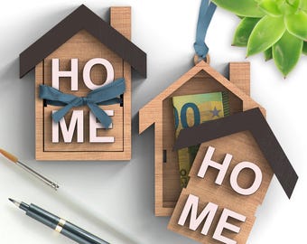 May include: Two wooden house-shaped boxes with the word "HOME" spelled out on the front. The top of the box is open and a blue ribbon is tied around it. The other box has a euro bill inside.