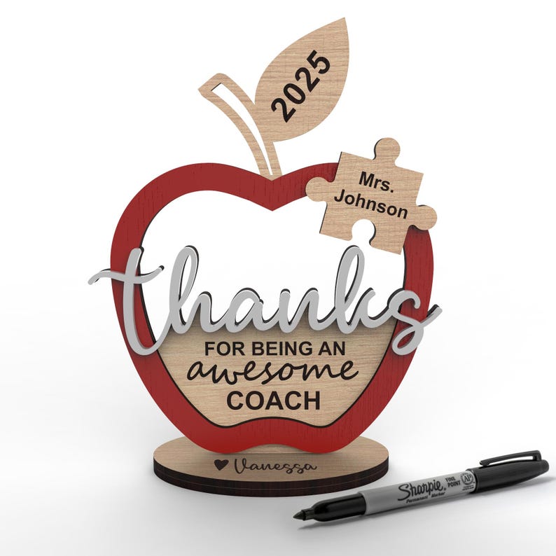 May include: A wooden apple-shaped award with a red outline and the words "thanks for being an awesome coach" on it. The apple has a leaf with the year 2025 on it and a puzzle piece with the text "Mrs. Johnson" on it. The base of the award has the name "Vanessa" on it.