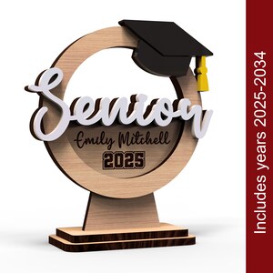 May include: Wooden senior graduation award with a graduation cap on top. The award has a circle in the middle with the word "Senior" in white letters and the text "Emily Mitchell 2025" below it.