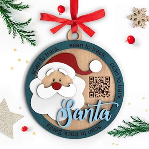 May include: A wooden Christmas bauble with a teal blue border and a Santa Claus face in the centre. The bauble has a QR code and the text "scan to track Santa" repeated around the edge.