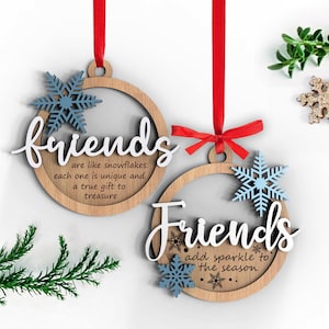 Puede incluir: Dos adornos navideños de madera con la palabra "Friends" escrita en ellos. Un adorno tiene el texto "are like snowflakes: each one is unique and a true gift to treasure." El otro adorno tiene el texto "add sparkle to the season". Ambos adornos tienen decoraciones de copos de nieve azules.