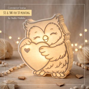 Puede incluir: Lámpara con forma de búho luminoso sosteniendo un corazón. Fabricada con material claro, emite un brillo cálido. El texto "STL & 3MF FOR 3D PRINTING" es visible. Un objeto decorativo.