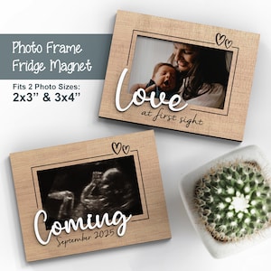Puede incluir: Dos marcos de fotos de madera con un imán en la parte posterior. El marco superior tiene el texto "Love at first sight" y un diseño de corazón. El marco inferior tiene el texto "Coming September 2025" y un diseño de corazón.