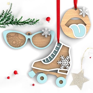 May include: Three wooden Christmas ornaments: a pair of blue sunglasses with a snowflake design, a blue roller skate with a snowflake design, and a red and blue lips ornament with a tongue sticking out.