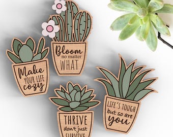 May include: Four wooden succulent plant ornaments with inspirational quotes. The quotes are "Bloom no matter what", "Make your life cozy", "Thrive don't just survive", and "Life's tough but so are you".