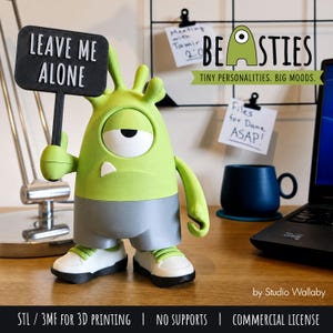 May include: A lime green, one-eyed monster figurine with a single white tooth, wearing grey shorts and white sneakers. The figure holds a black sign with the white text LEAVE ME ALONE. The text BEASTIES TINY PERSONALITIES BIG MOODS is visible.
