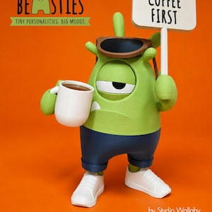 May include: A green one-eyed monster figurine wearing dark blue shorts, white sneakers, and brown sunglasses on its head. It holds a white coffee mug in one hand and a white sign that reads COFFEE FIRST in the other. The text BEASTIES TINY PERSONALITIES. BIG MOODS. appears above.