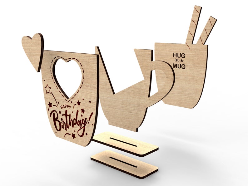 May include: Wooden craft kit to make a mug shaped birthday card. The card features a heart-shaped cutout and the text "Happy Birthday!" and "Hug in a Mug".