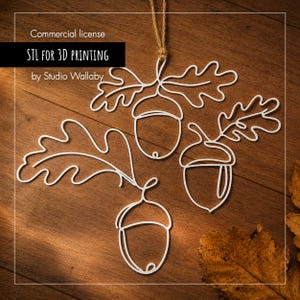May include: A white wire-frame wall hanging featuring three stylised acorns with attached oak leaves. The design is composed of continuous lines forming the shapes of the nuts and foliage. Text on the image reads: Commercial license STL FOR 3D PRINTING by Studio Wallaby.