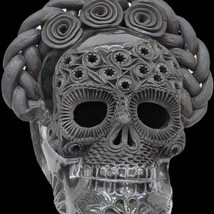 Puede incluir: Cráneo de cerámica negra con intrincados diseños florales y una corona trenzada. El cráneo tiene una cara detallada con cuencas de los ojos, una nariz y una boca.