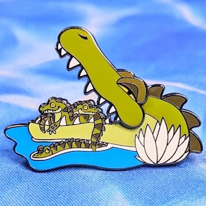 May include: A green alligator with its mouth open, sitting on a blue lily pad with two smaller alligators. The larger alligator has a white lily pad behind it.