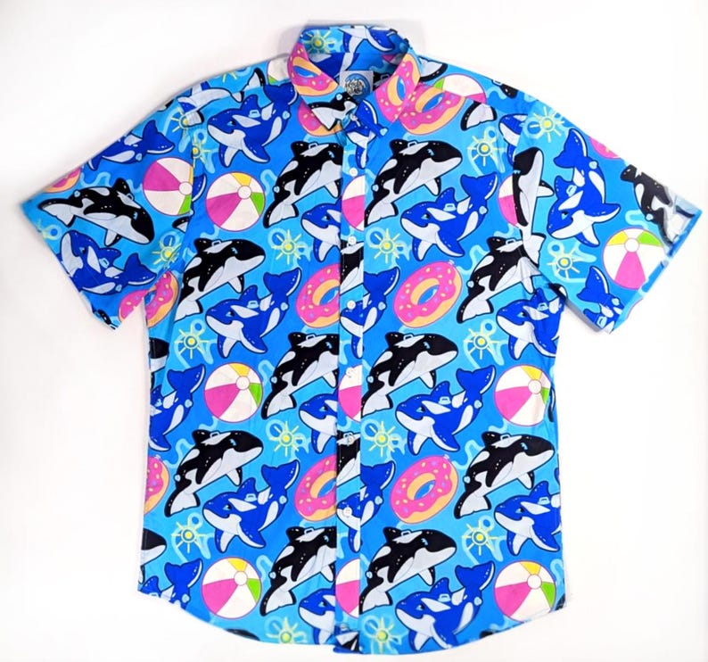 May include: A blue short-sleeved button-down shirt with a colorful print of orcas, donuts, and beach balls.