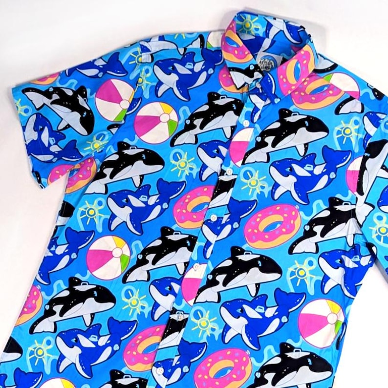 May include: A blue short-sleeved button-down shirt with a colorful print of orcas, donuts, and beach balls.
