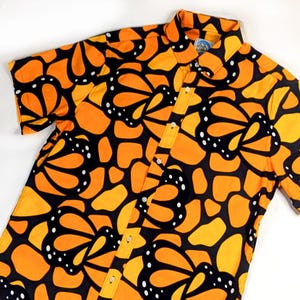 May include: A short-sleeved button-down shirt with a black background and a pattern of orange and yellow monarch butterflies.