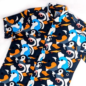 Könnte beinhalten: Ein kurzärmeliges Hemd mit Knöpfen und einem Muster aus schwarzen, weißen, orangen und blauen Pinguinen.