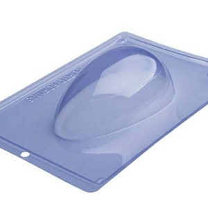May include: A clear plastic mold for making chocolate eggs. The mold is rectangular with a single egg-shaped cavity. The mold is labeled "SWIRLO CHOCO".