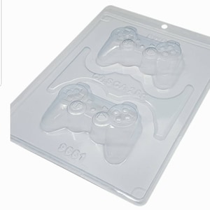 May include: A clear plastic mold for making chocolate game controllers. The mold has two cavities, each shaped like a video game controller. The mold is labeled "9661" and "CASCA 2009".