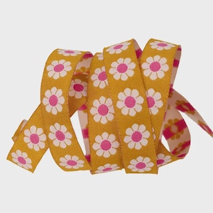 May include: Mustard yellow ribbon with a repeating pattern of white daisies with pink centers. The ribbon is curled and folded, showcasing the floral design. The ribbon is likely used for crafts, gift wrapping, or decorative purposes.