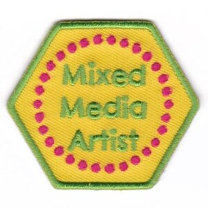 May include: Yellow hexagonal patch with a green border and pink dots around the edge. The text "Mixed Media Artist" is embroidered in green on the patch.