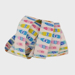 May include: White ribbon with a repeating pattern of colorful soda bottles in pink, yellow, and blue. The ribbon is curled and features the words "Fizzle", "Soda", and "Lemon".