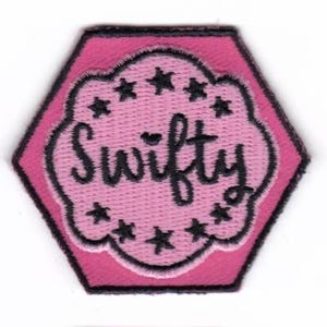May include: Pink hexagonal patch with a black outline. The center features a pink cloud with a black outline and the word "Swifty" written in black cursive. The cloud is decorated with black stars.