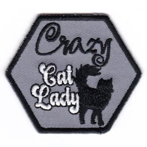 May include: A gray hexagonal patch with black and white embroidery. The text "Crazy Cat Lady" is embroidered in white with a black cat silhouette below it.