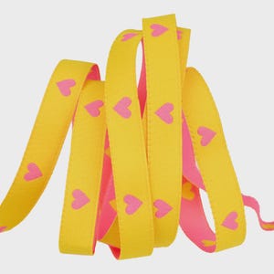 May include: Yellow ribbon with pink hearts printed on the front. The ribbon is folded and layered, revealing a pink underside. This decorative ribbon is suitable for crafts, gift wrapping, or other creative projects.