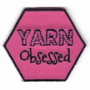 May include: Pink hexagonal patch with black embroidered text that reads "YARN Obsessed".
