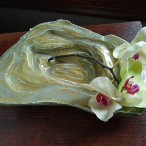 May include: A ceramic dish with a textured, green and blue glaze. The dish has a shallow, rounded shape and is decorated with a single branch of white orchids.