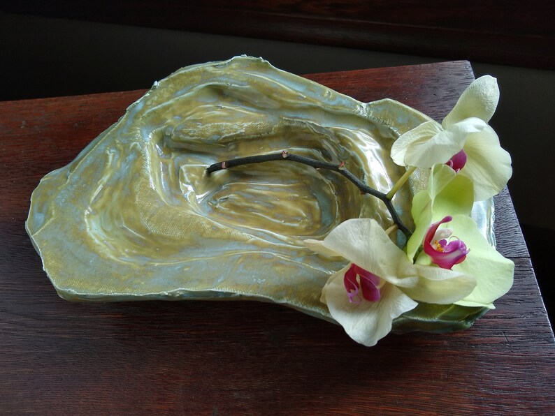 May include: A ceramic dish with a textured, green and blue glaze. The dish has a shallow, rounded shape and is decorated with a single branch of white orchids.