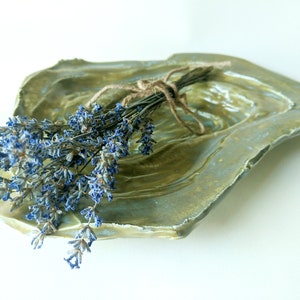 May include: A green ceramic dish with a textured surface, featuring a bouquet of dried lavender tied with twine.