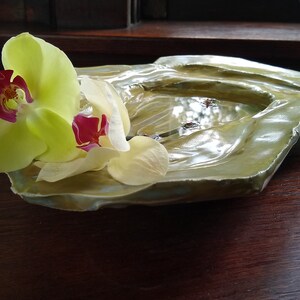 May include: A green ceramic dish with a rough, textured surface. The dish is decorated with a single yellow orchid with a red center.