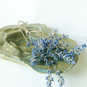 May include: A bunch of dried lavender flowers tied with twine, resting in a green ceramic dish with a textured surface.
