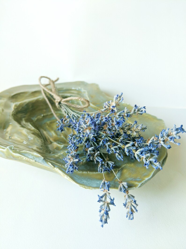 May include: A bunch of dried lavender flowers tied with twine, resting in a green ceramic dish with a textured surface.