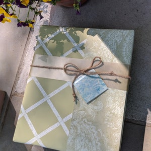 May include: A gift wrapped in green and white patterned paper with a brown twine bow and a blue tag.
