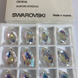 May include: A box of 12 clear crystal teardrop-shaped beads with iridescent rainbow colors. The box is labeled "Swarovski" and "Aurora Boreale".