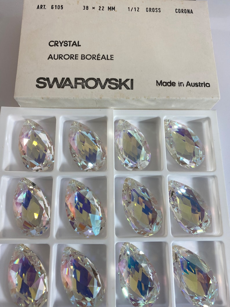 May include: A box of 12 clear crystal teardrop-shaped beads with iridescent rainbow colors. The box is labeled "Swarovski" and "Aurora Boreale".