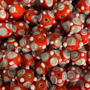 May include: A collection of red and white glass beads with a swirl pattern. The beads are round and have a textured surface.