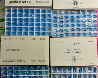 May include: Four boxes of light sapphire Swarovski crystals. The boxes are labeled with the product number, size, and color. The crystals are in a variety of sizes and shapes.