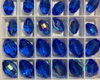 May include: A close-up of a white plastic container filled with 42 blue glass beads. The beads are oval shaped and have a faceted design.